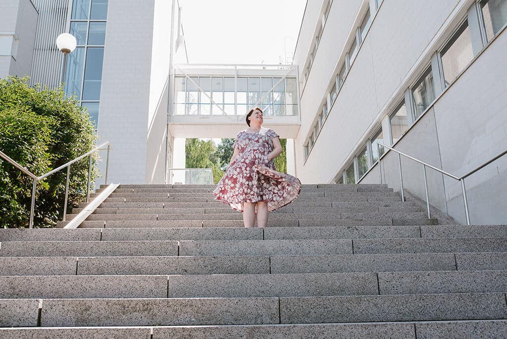 Nainen seisoo ulkona keskellä korkeita portaita ja heiluttaa hameen helmoja.